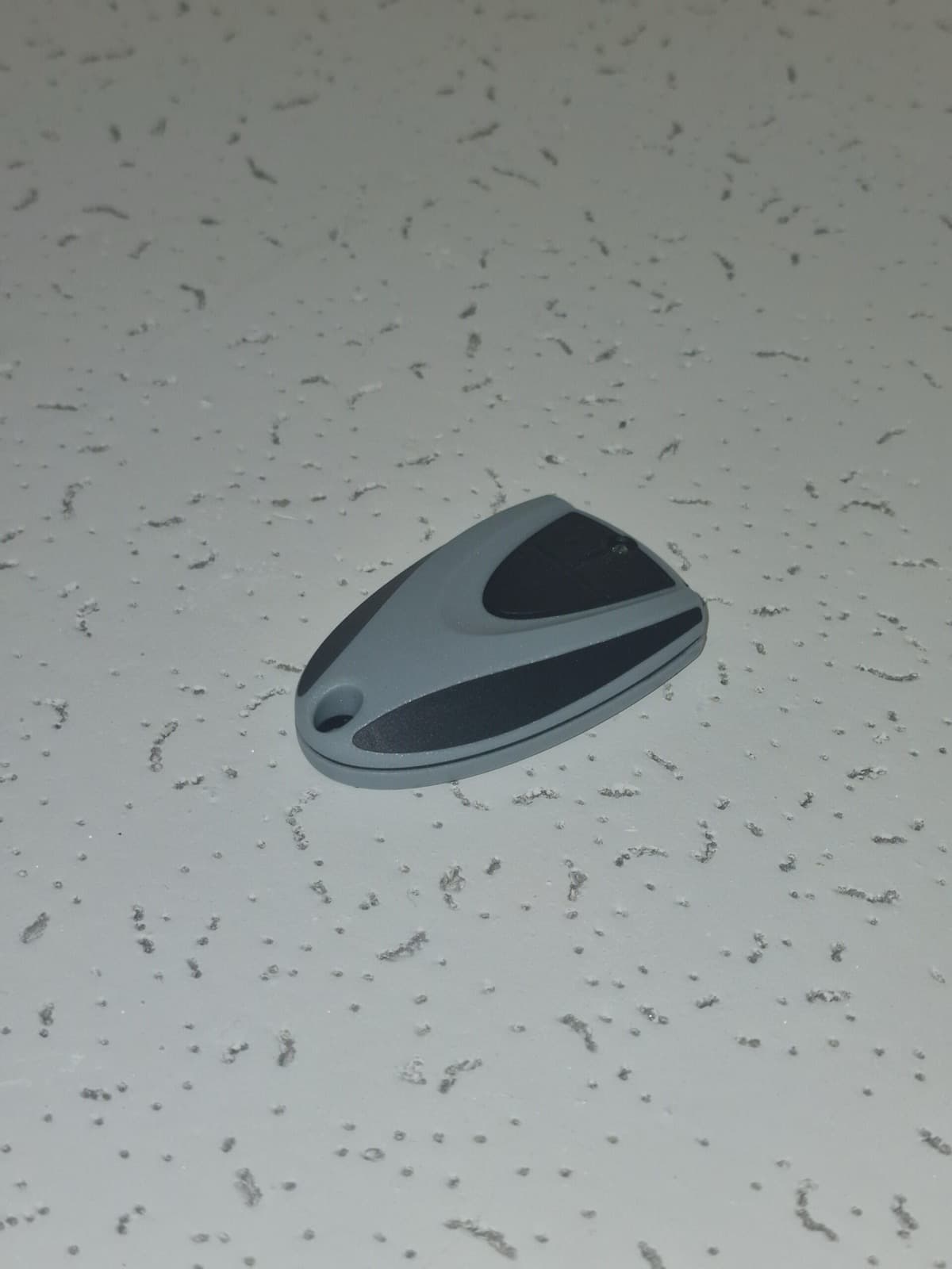 Guscio bicolore grigio e nero di un telecomando, con foro per anello.